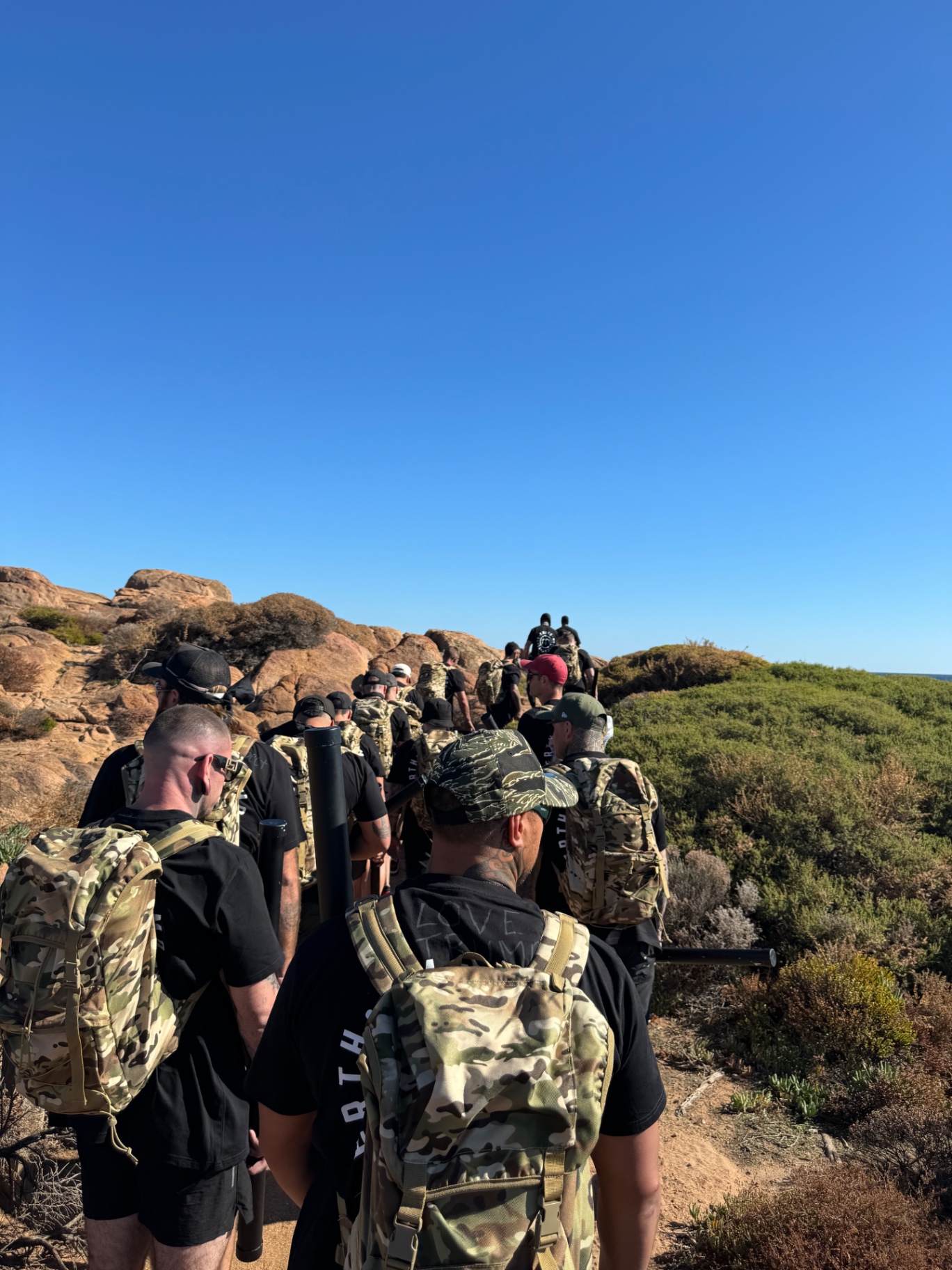 A long line of Amend Movement men with packs walking a coastal trail
